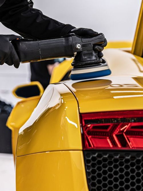 A person is polishing a yellow sports car with a machine.