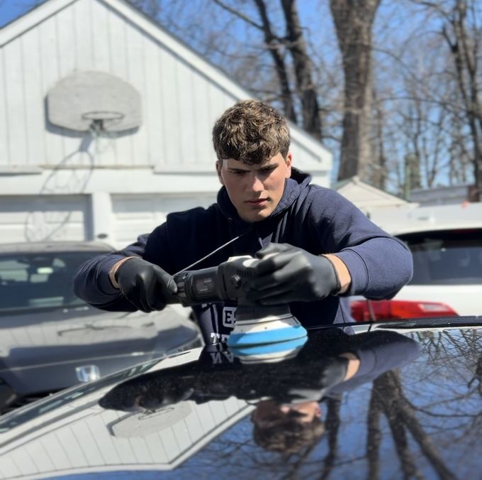 A young man is polishing the hood of a car.