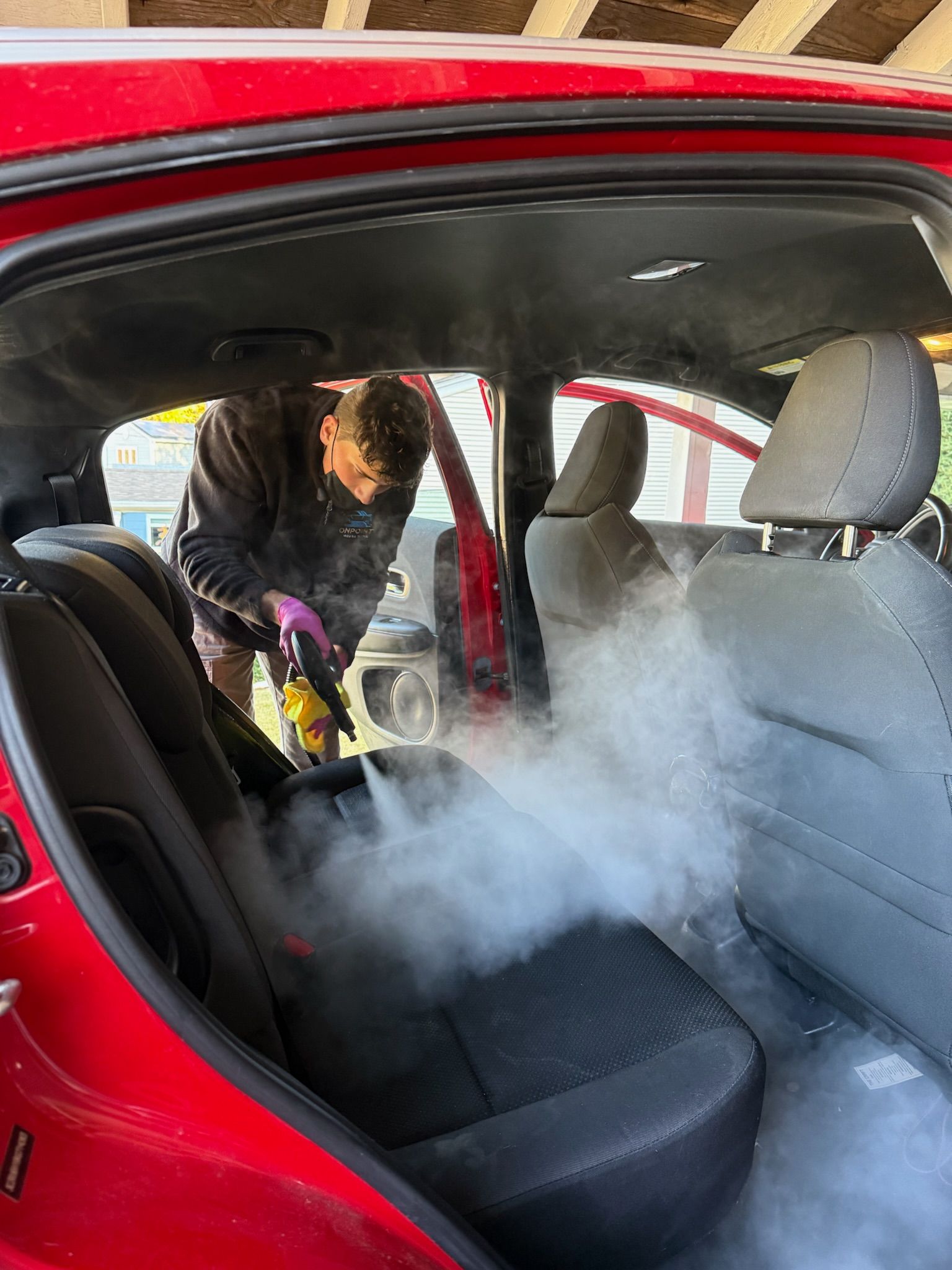 A person wearing black gloves is polishing the hood of a red car.