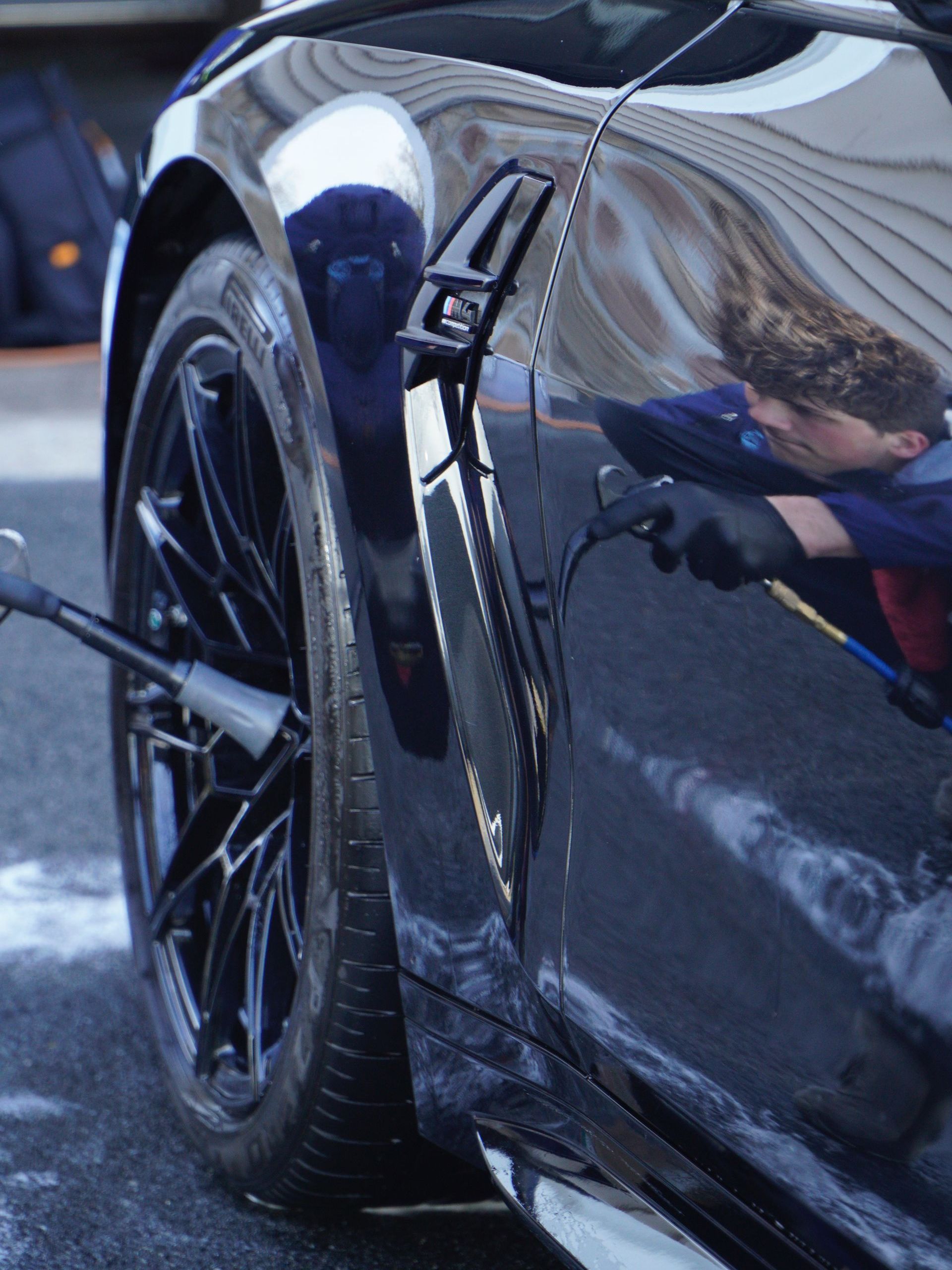 A person is cleaning a blue car with an orange towel
