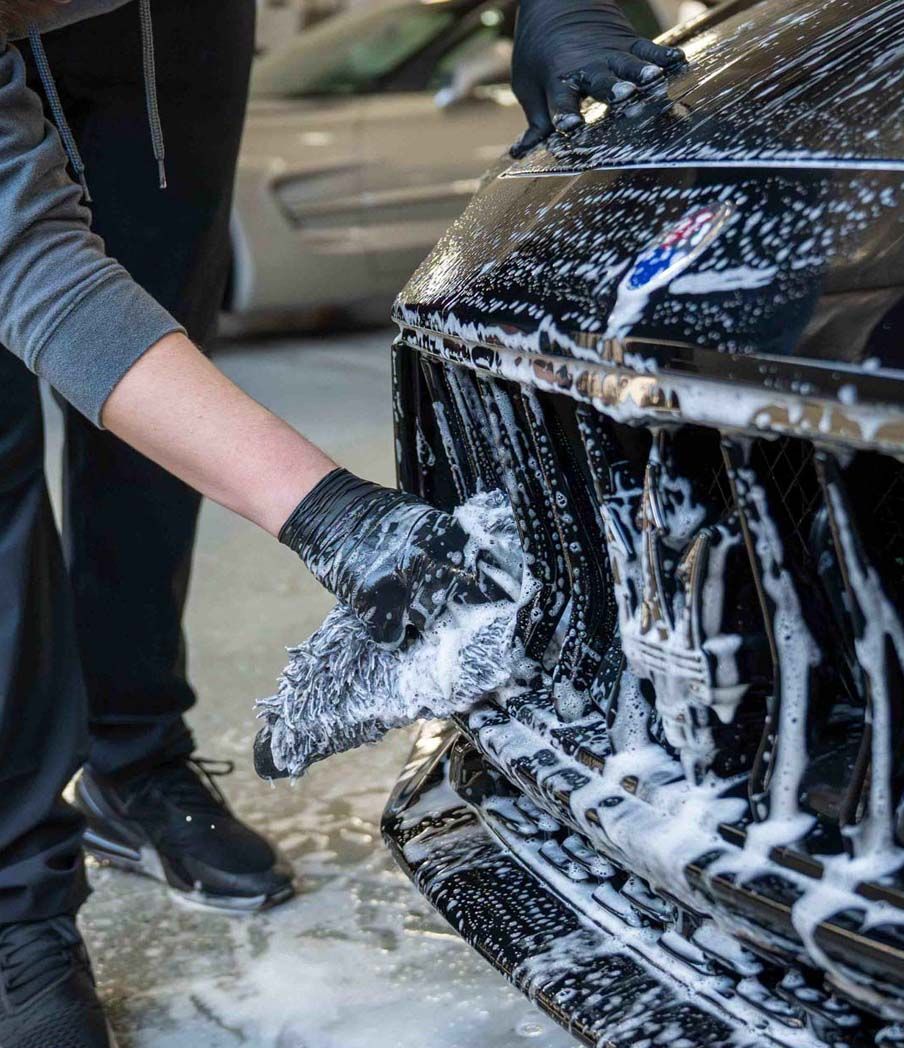 A person is washing a black car with soap and water.