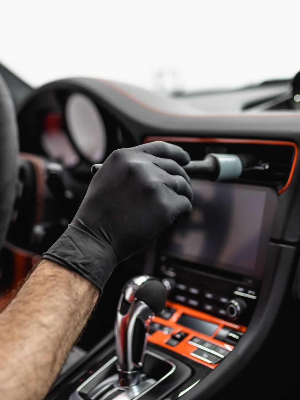 A man wearing black gloves is cleaning the dashboard of a car.