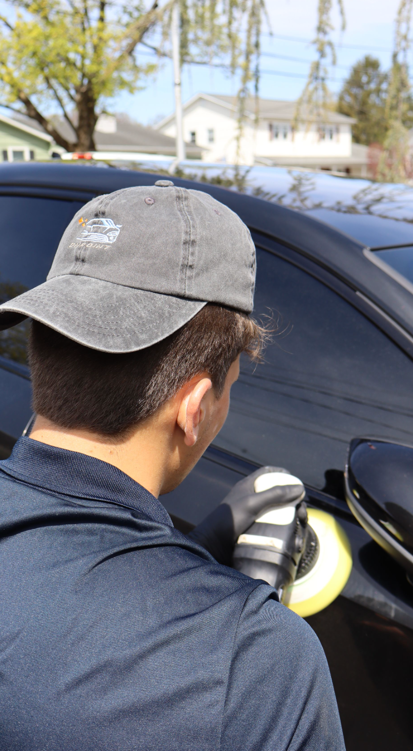A man is polishing the hood of a yellow sports car.