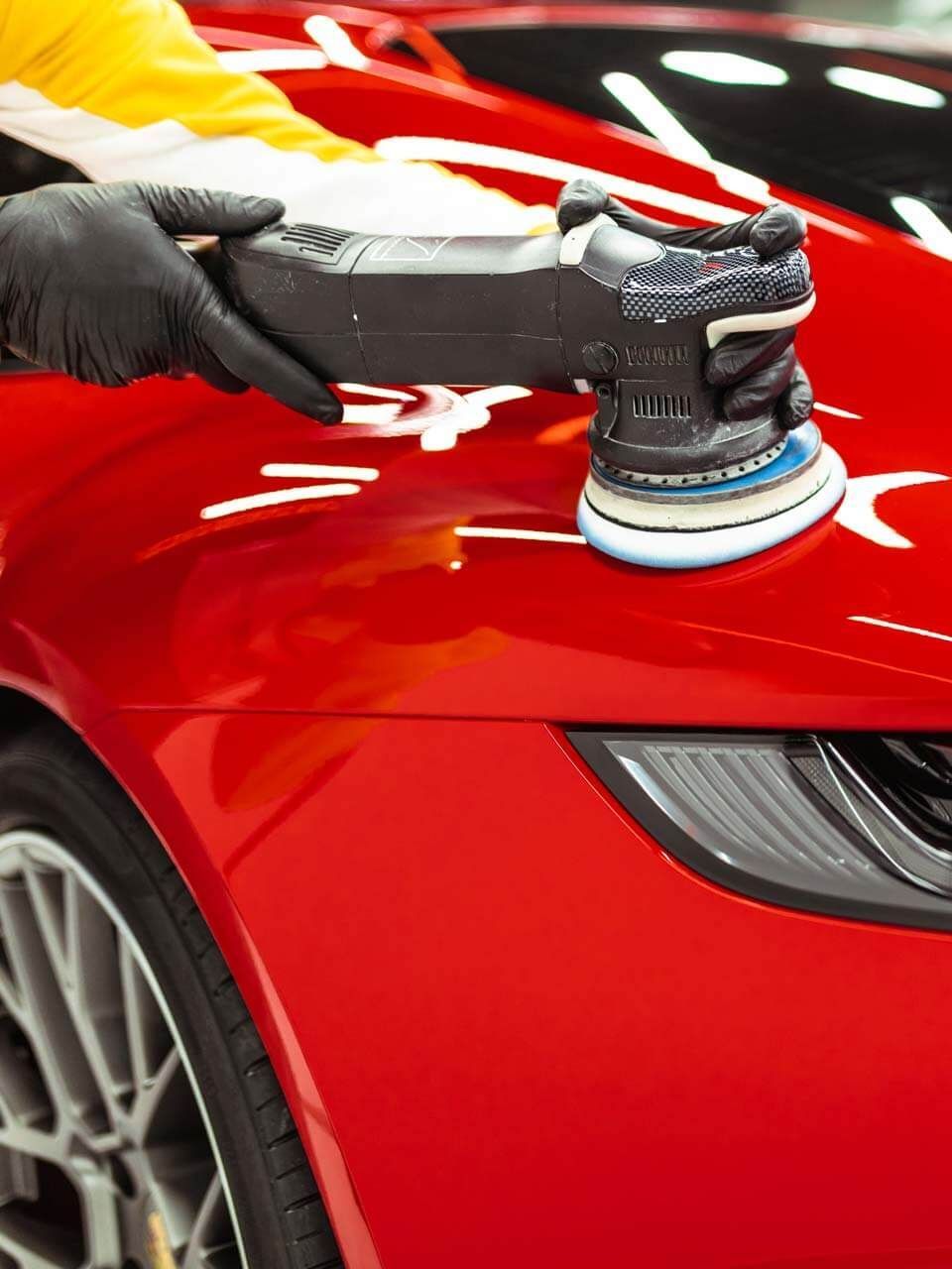 A person is polishing a red car with a machine.