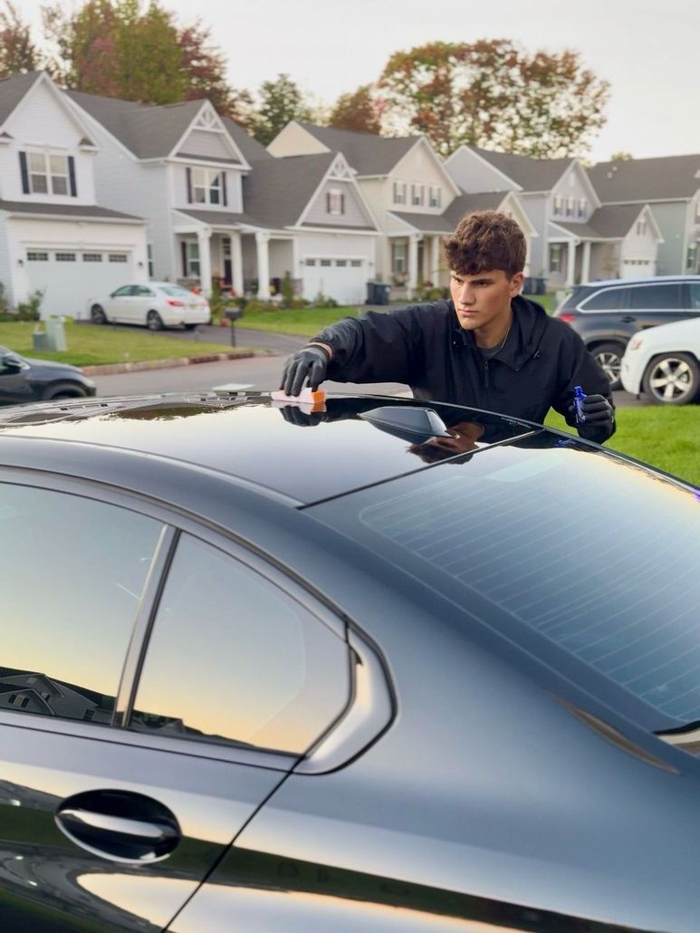 A person wearing black gloves is polishing a black car
