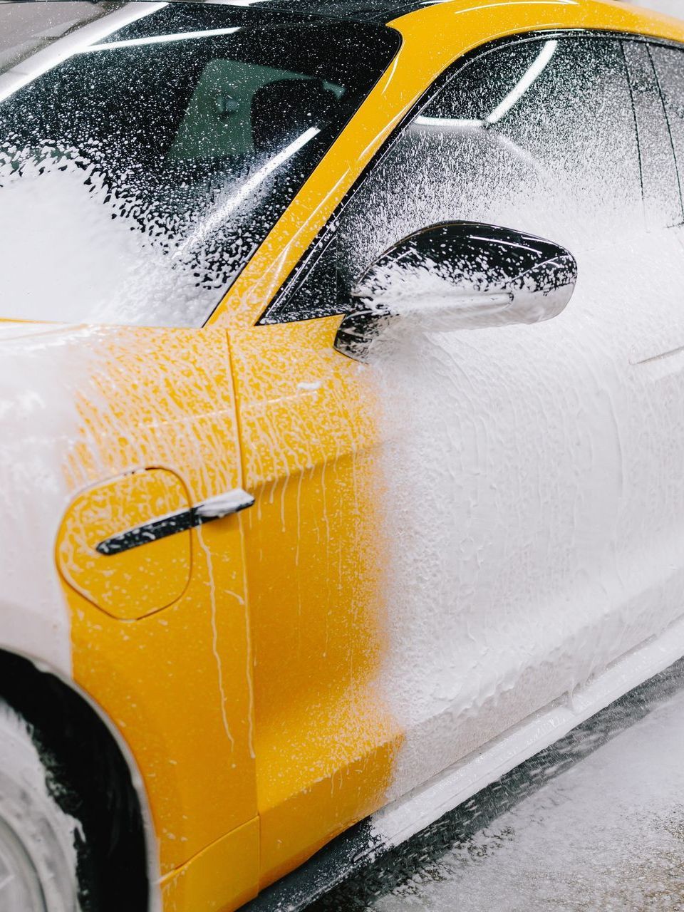 A person wearing black gloves is polishing a black car