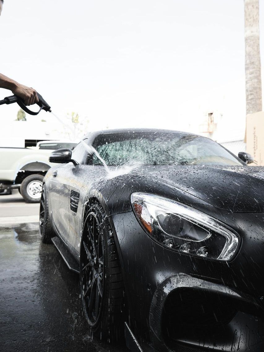 A man is washing a black sports car with a high pressure washer.