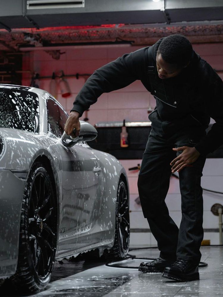 A man is cleaning the wheel of a black car with a sponge.
