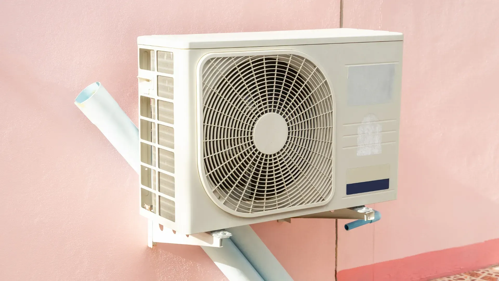 A white air conditioner is mounted on a pink wall.