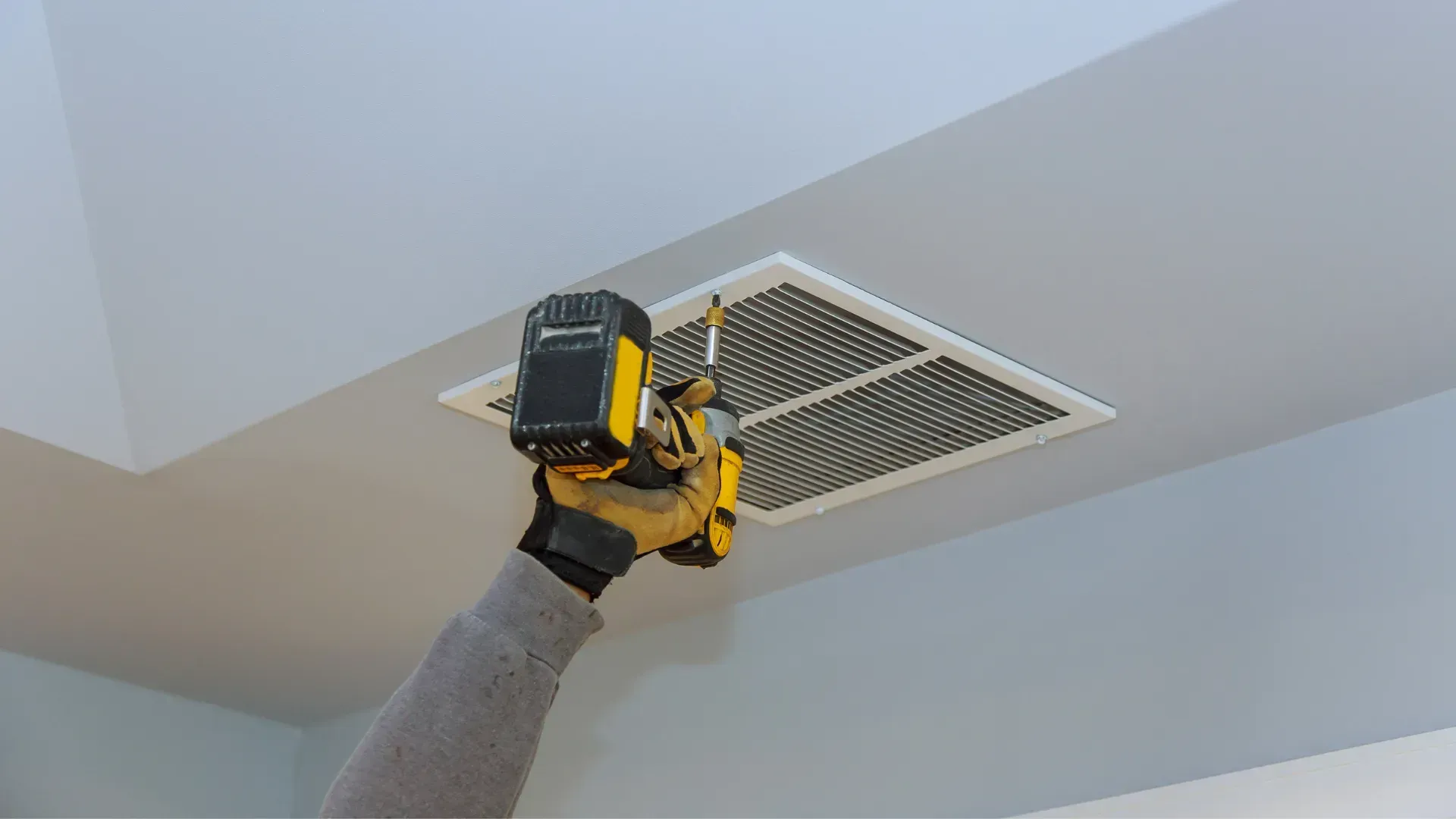 A person is using a drill to fix an air vent on the ceiling.