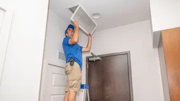 A man is hanging a filter from the ceiling of a room.