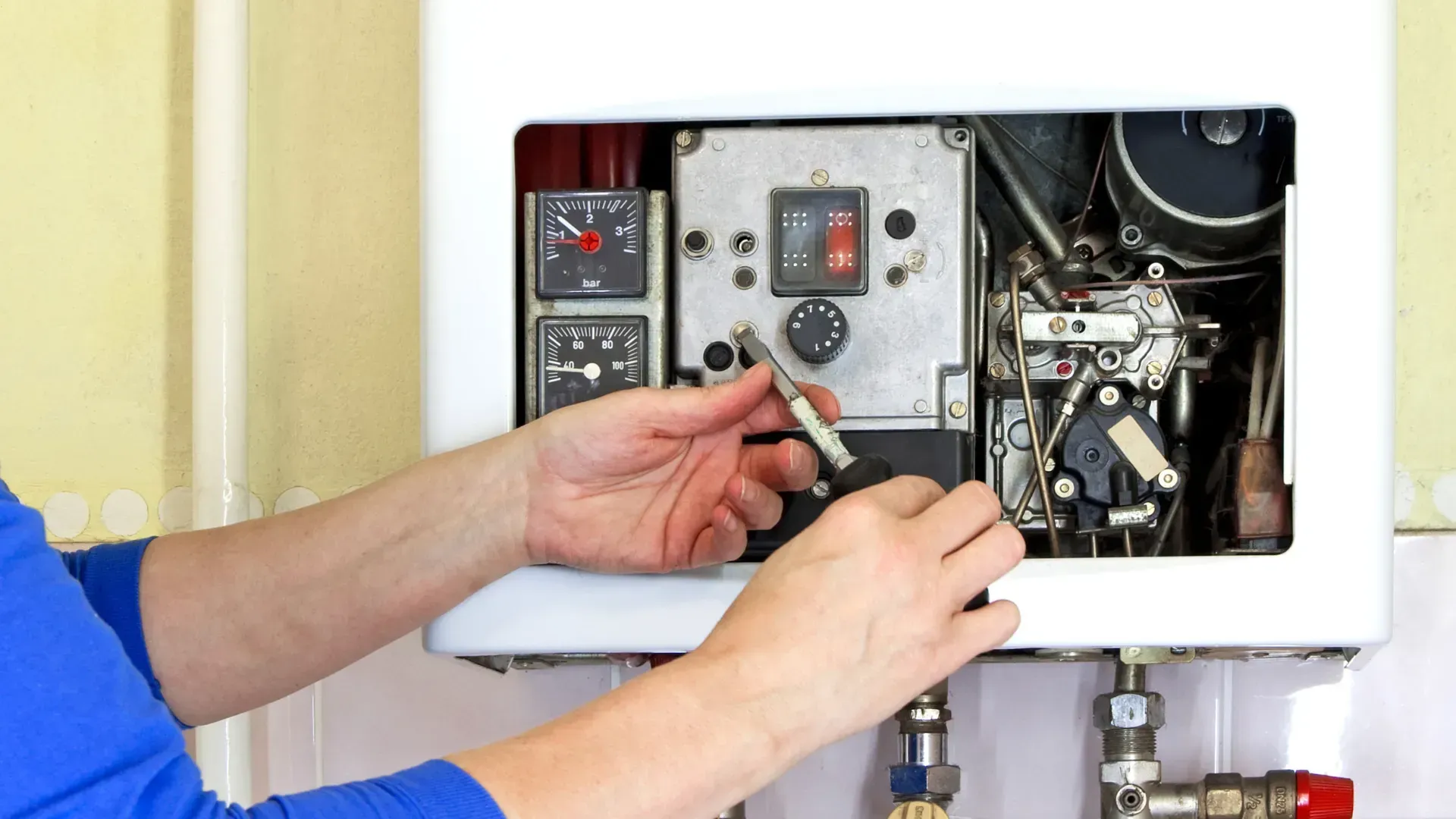 A person is fixing a boiler with a screwdriver.