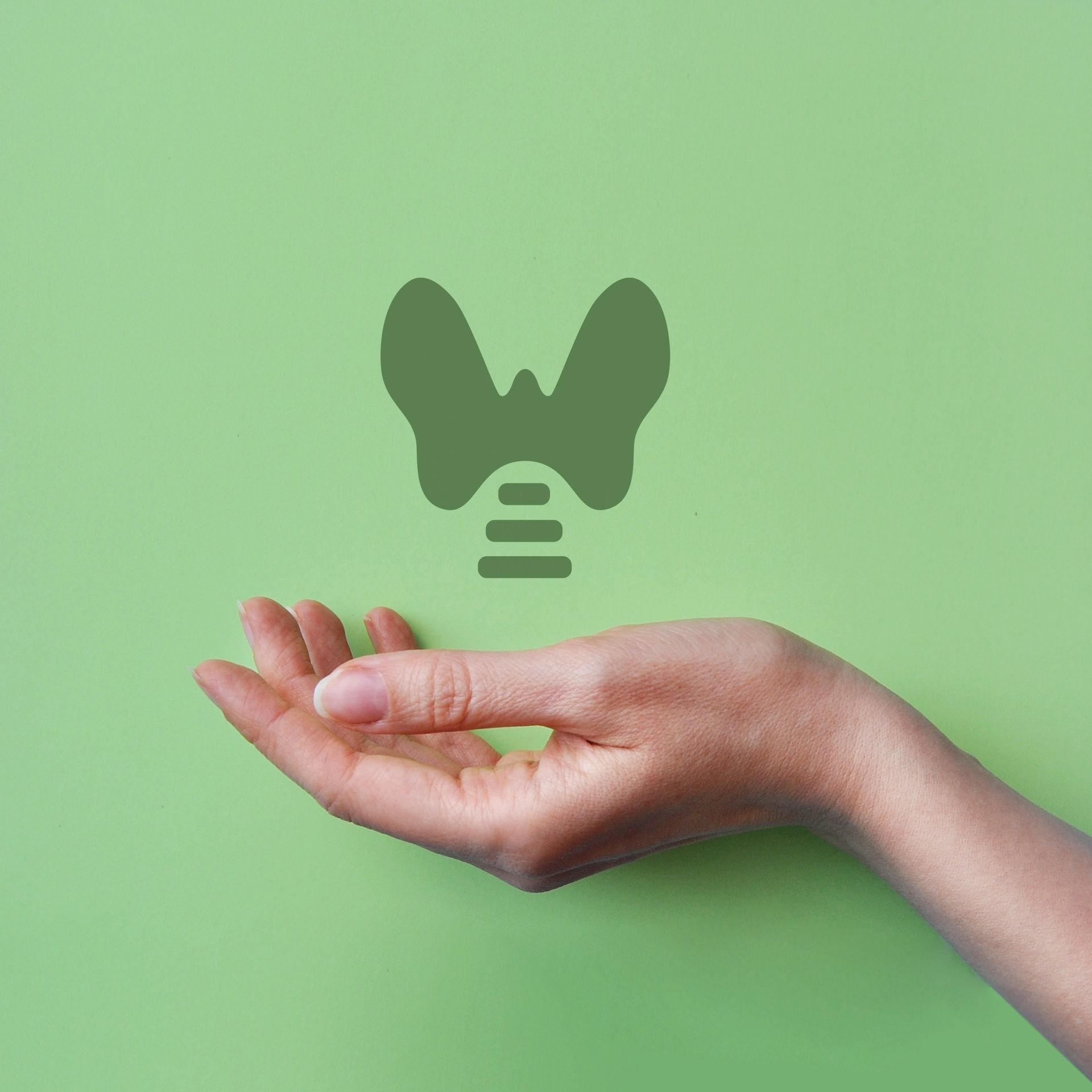 Hand holding a green thyroid gland icon against a solid green background.