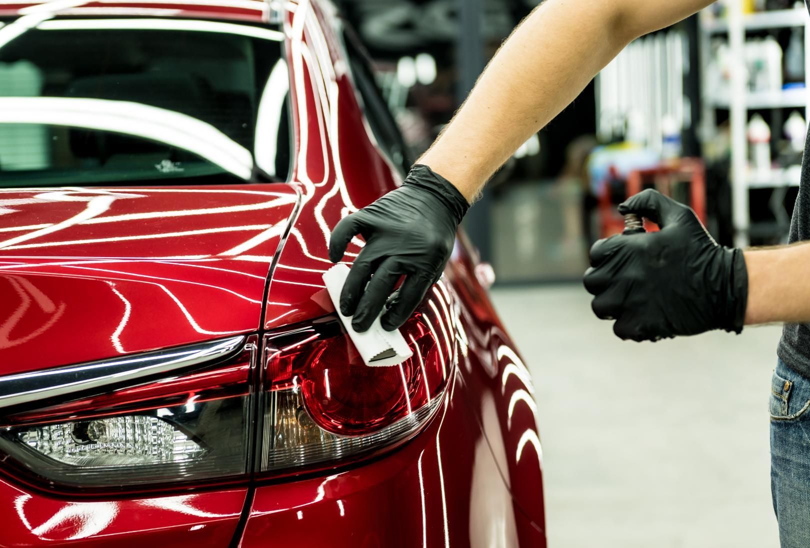 A person wearing black gloves is polishing a red car.