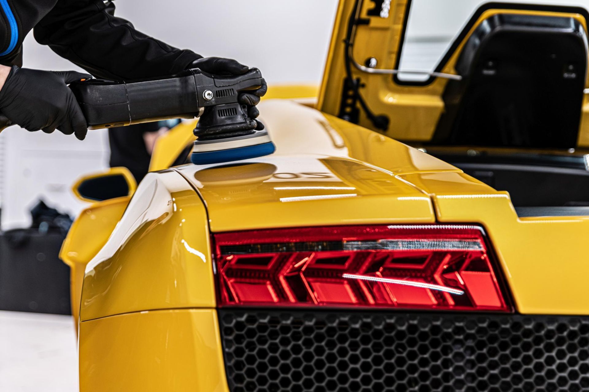 A man is polishing the hood of a yellow sports car.