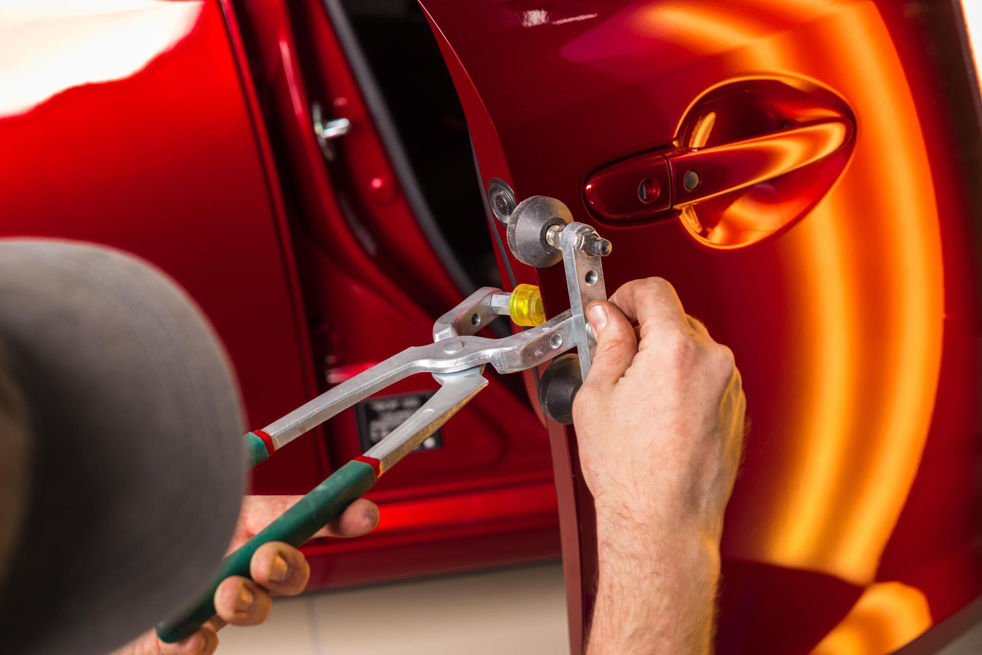 A man is working on a red car door with a pair of pliers.