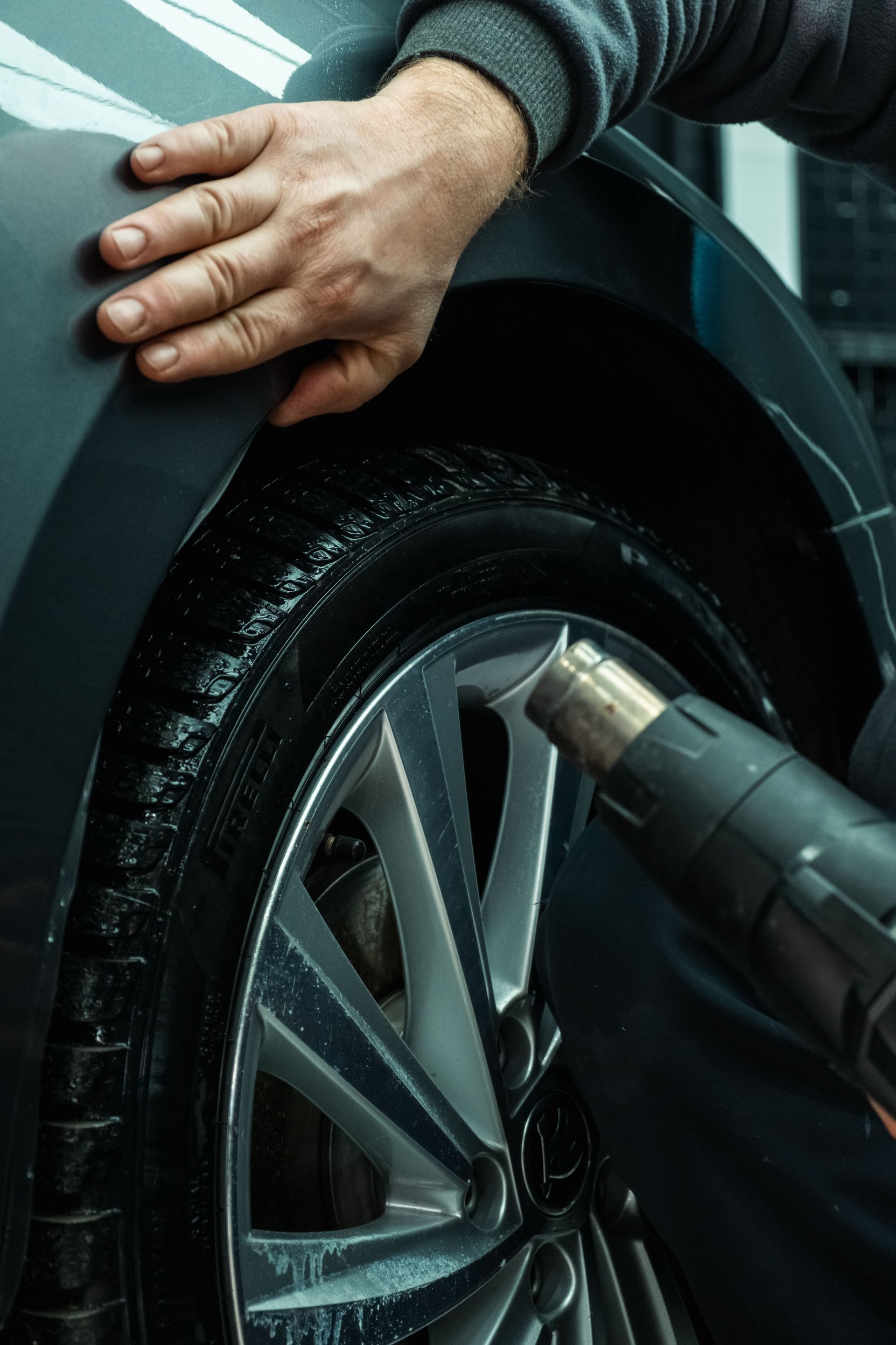 Hand cleaning a car wheel with a pressure washer nozzle spraying the tire