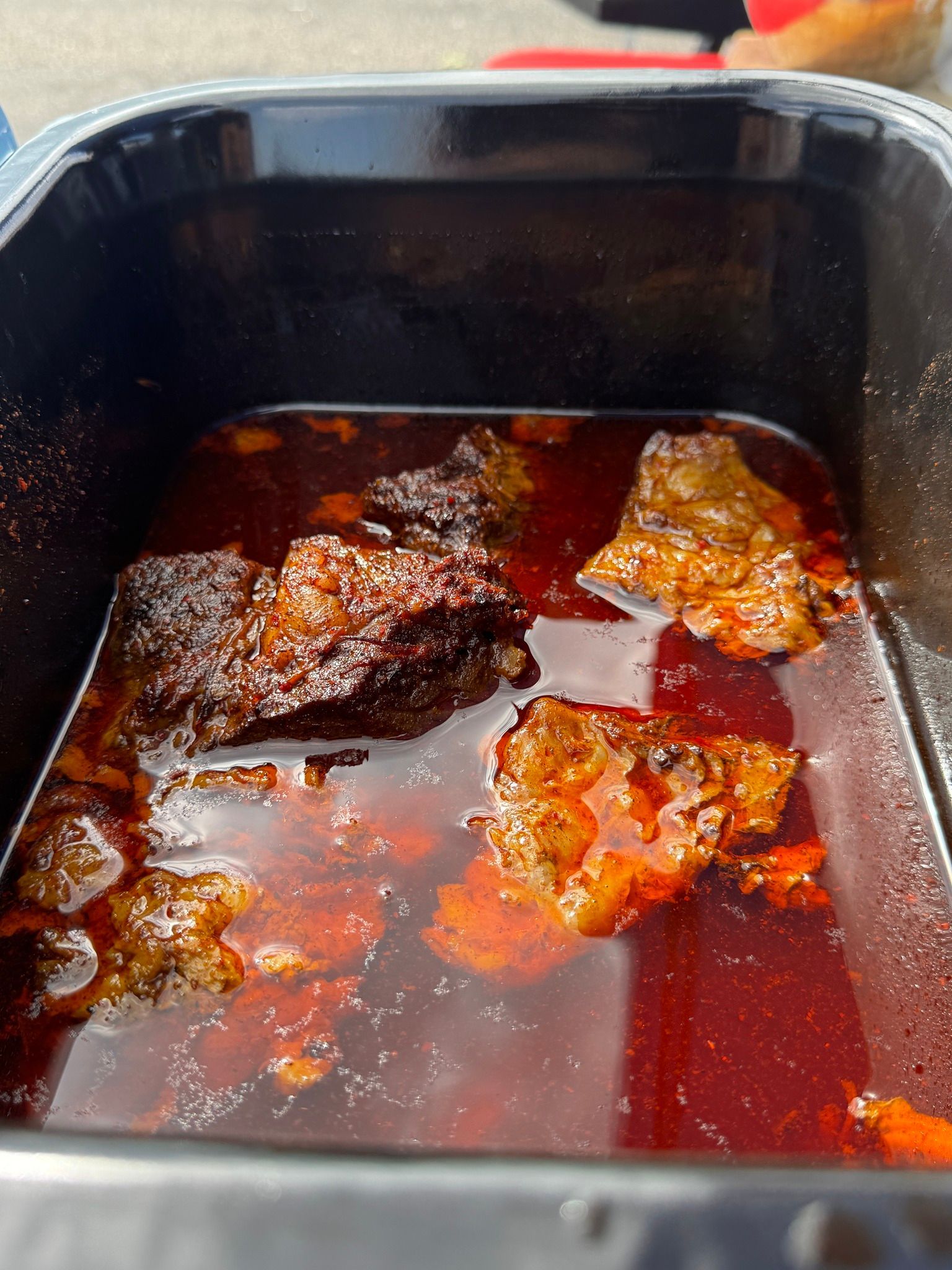 Chunks of dark, cooked meat in a dark reddish-brown sauce inside a black container.