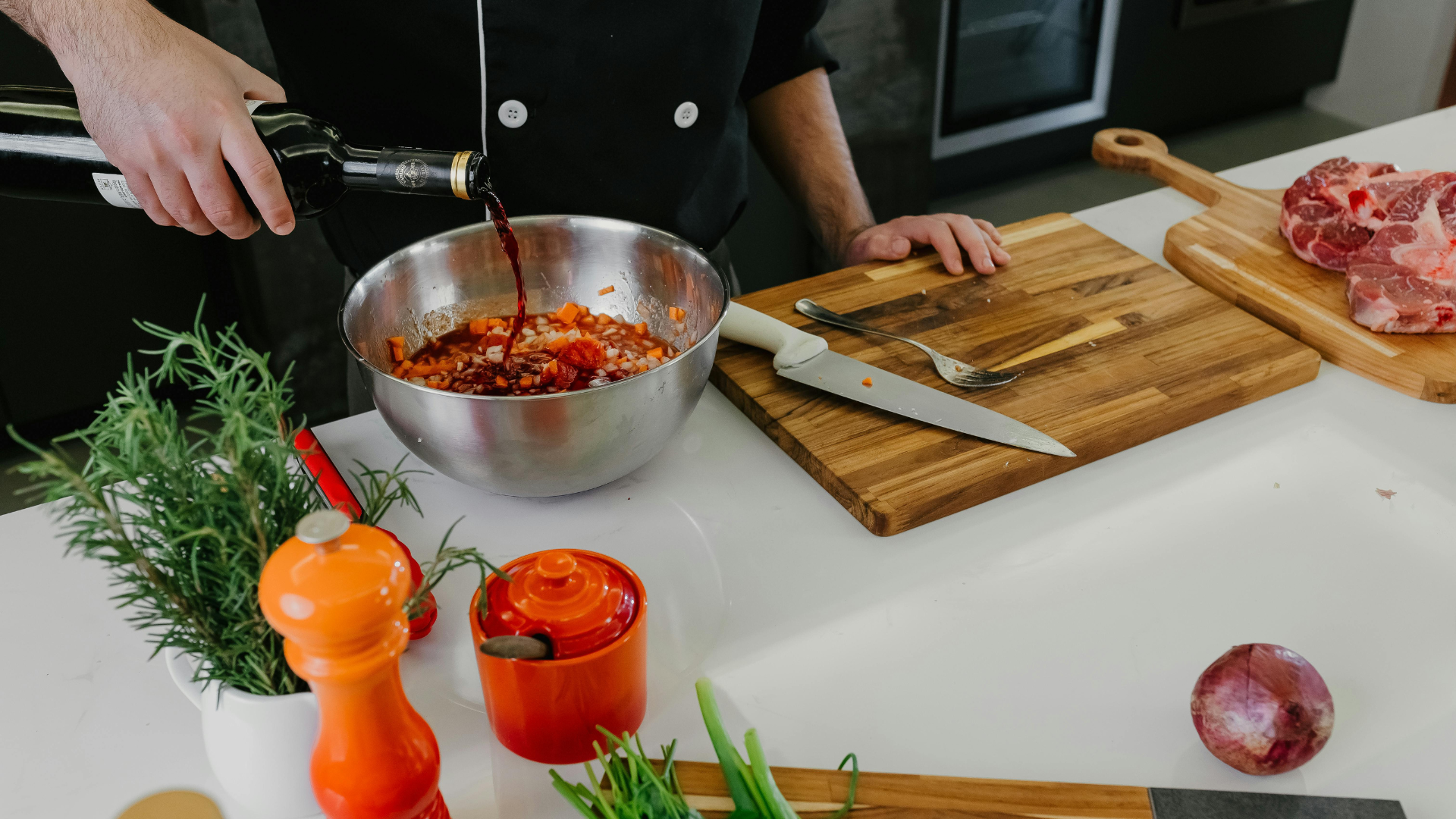 Chef pouring red wine into a bowl of ingredients on a kitchen counter.
