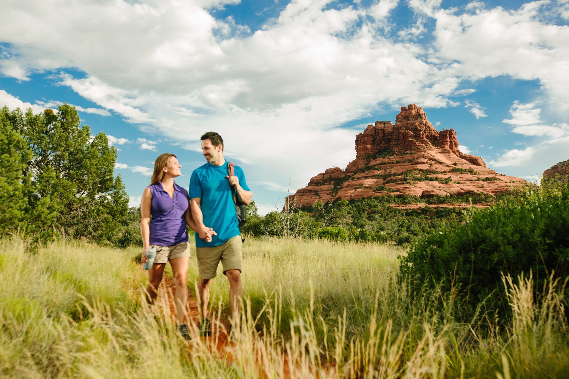 A man and a woman are walking in a field with a mountain in the background.