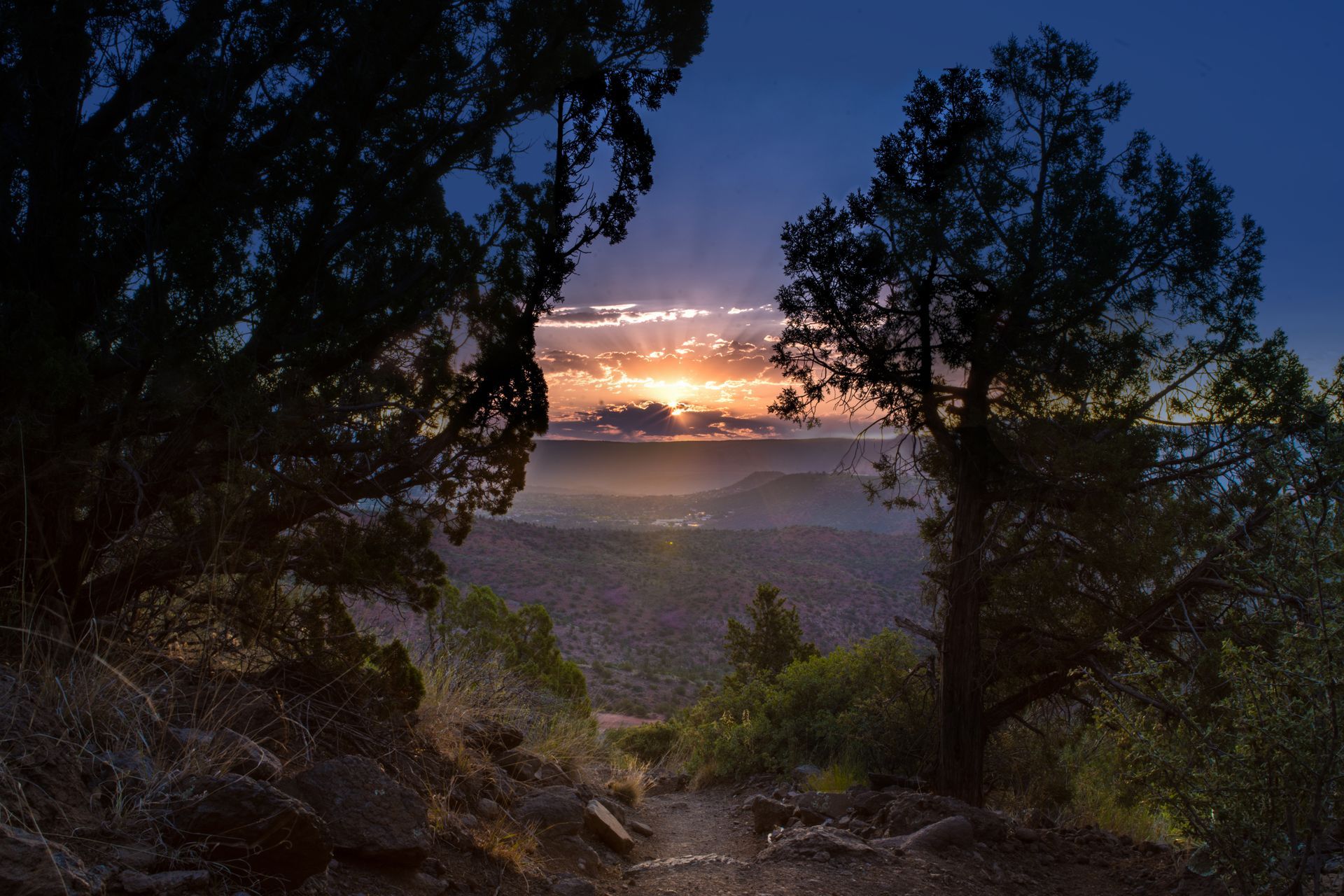 A sunset over a valley with trees in the foreground