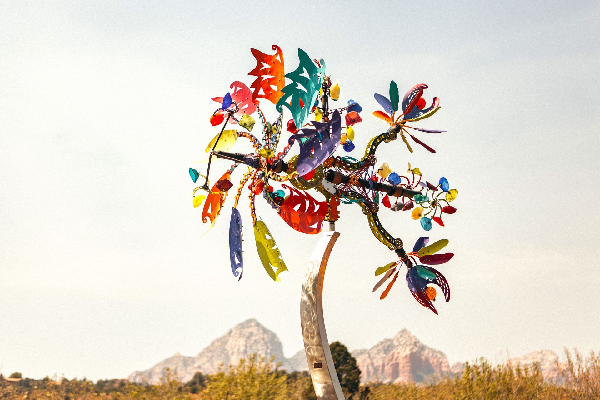 A colorful tree made out of plastic bottles in a field with mountains in the background.