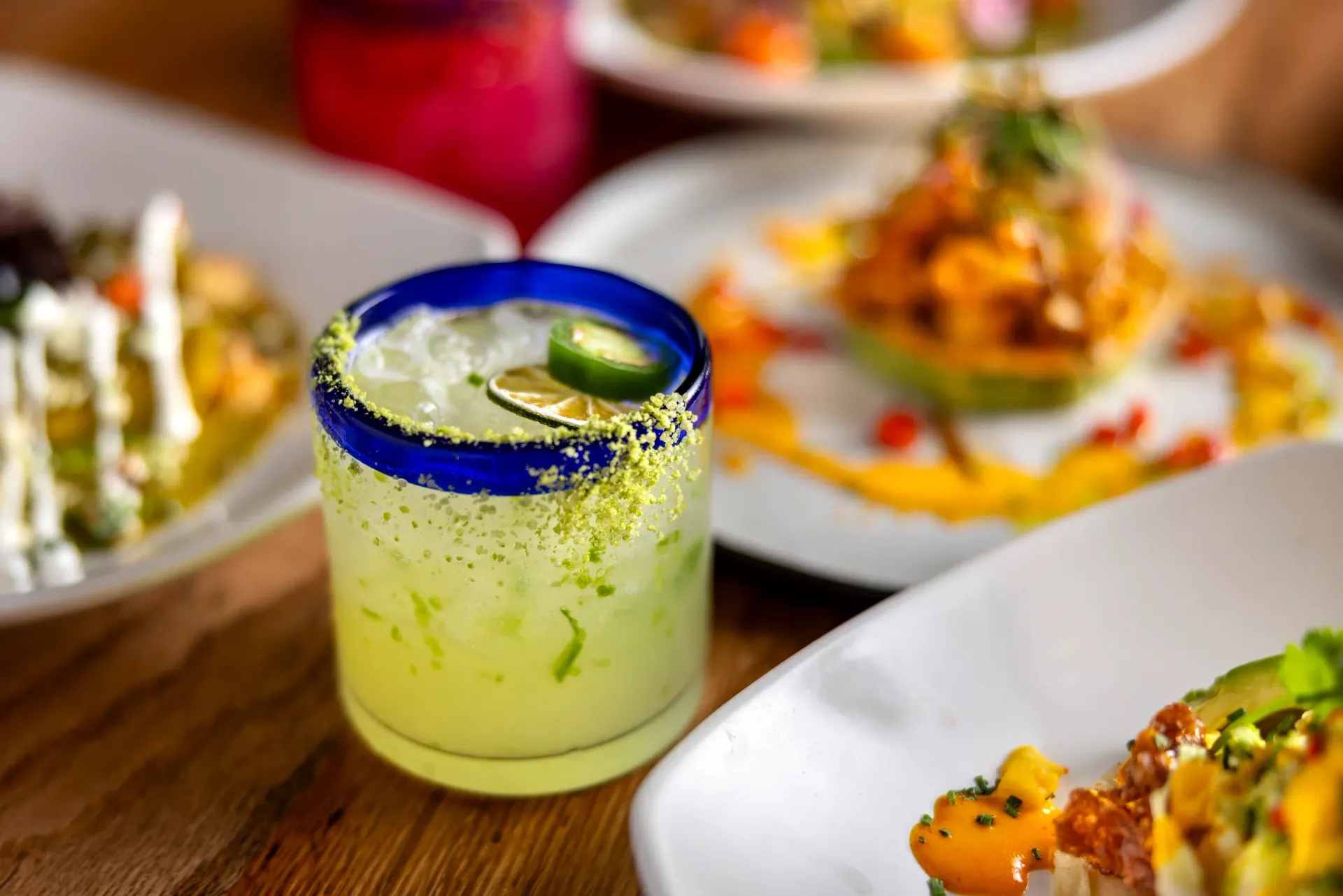 A margarita is sitting on a table next to plates of food.