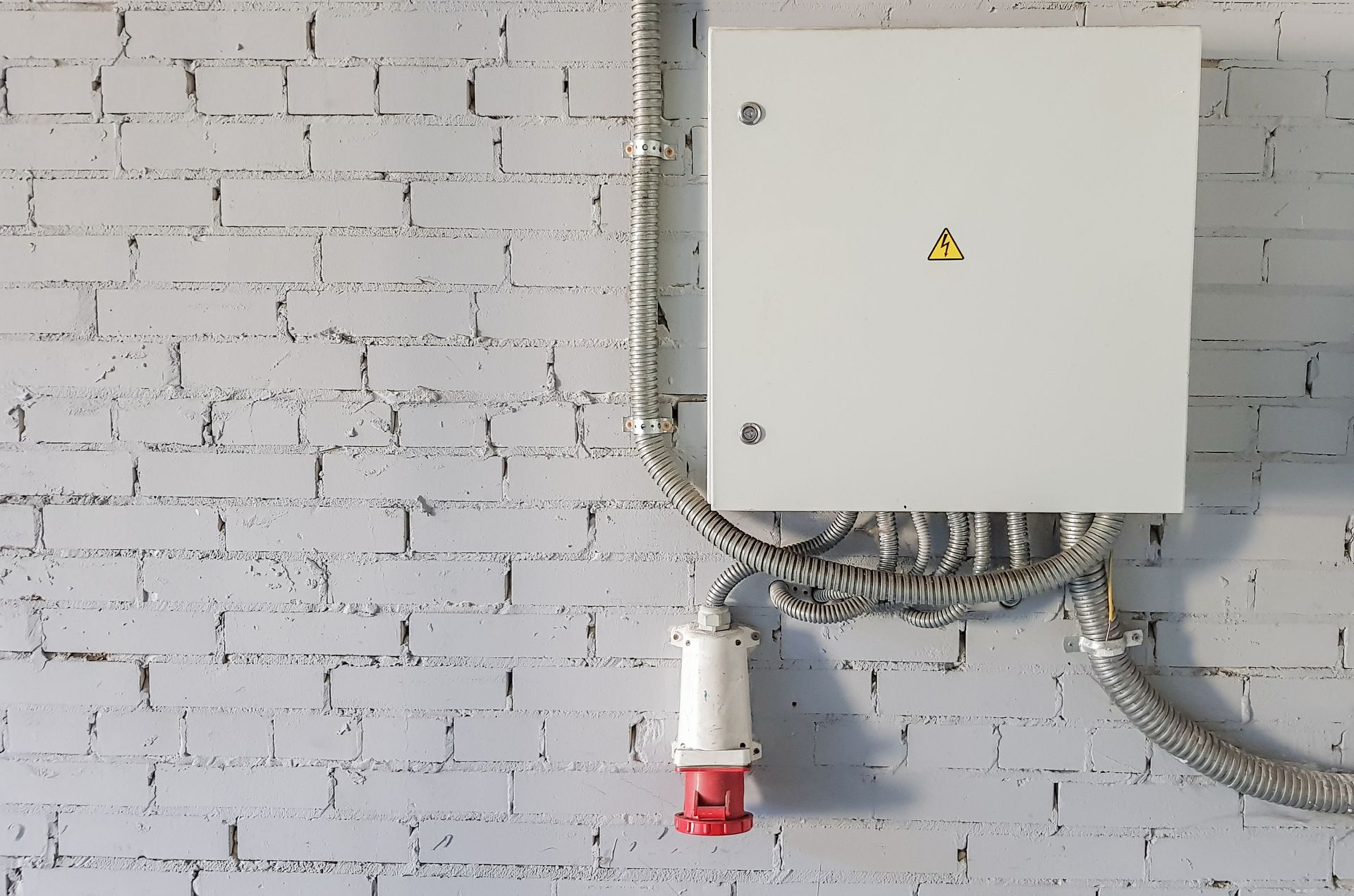A white box with a red plug attached to it is hanging on a white brick wall.