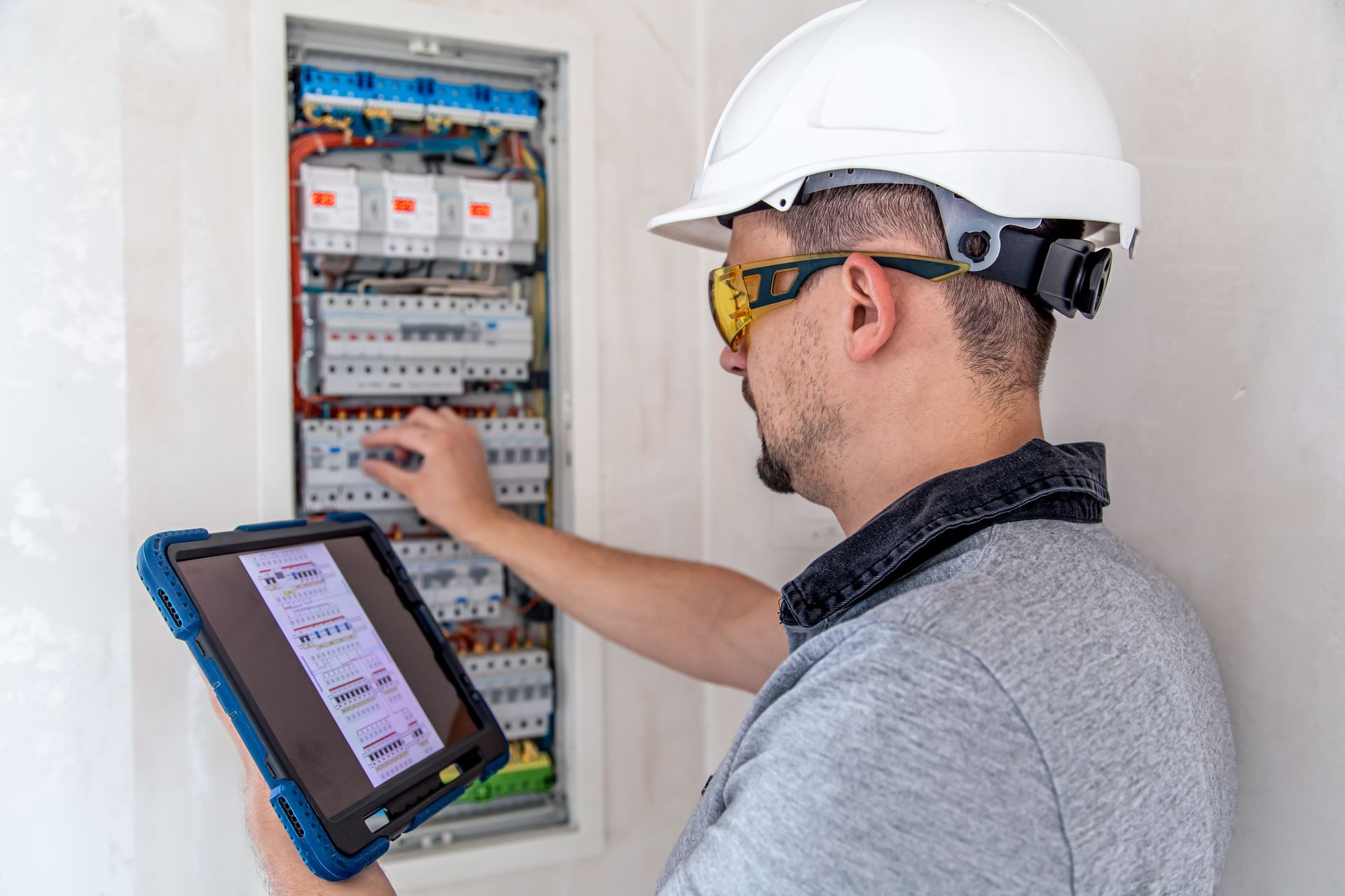 Electrician in safety gear, examining electrical panel with a tablet. Electrician in safety gear, examining electrical panel with a tablet.