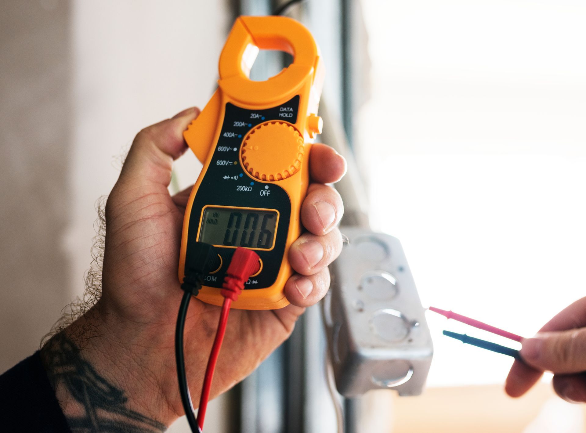 Person holding a yellow clamp meter, testing electrical wiring in a white junction box.