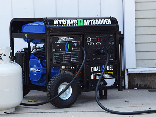A blue and black generator is connected to a propane tank.