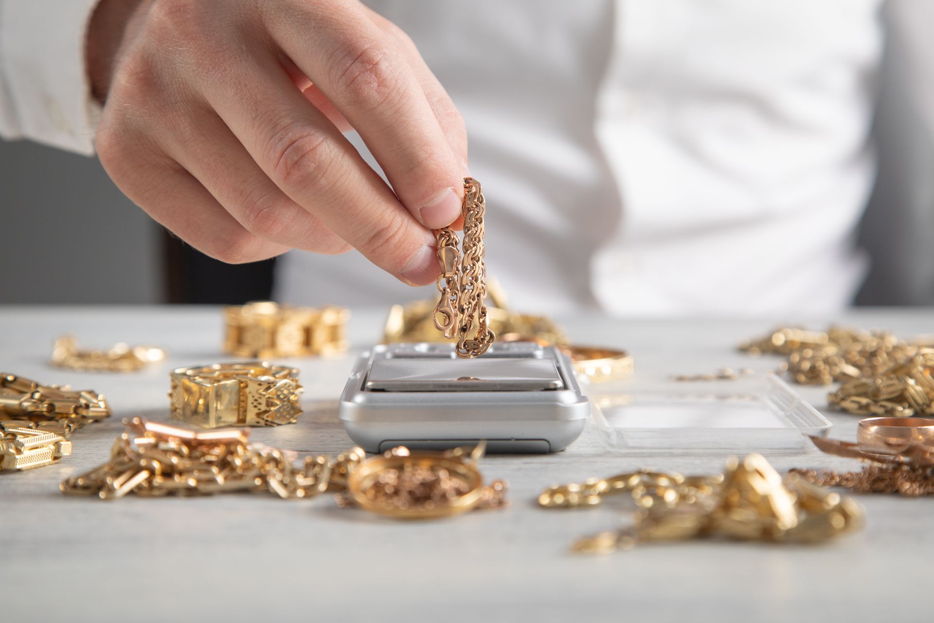 A jeweler weighing a gold chain on a scale beside piles of assorted gold jewelry for appraisal