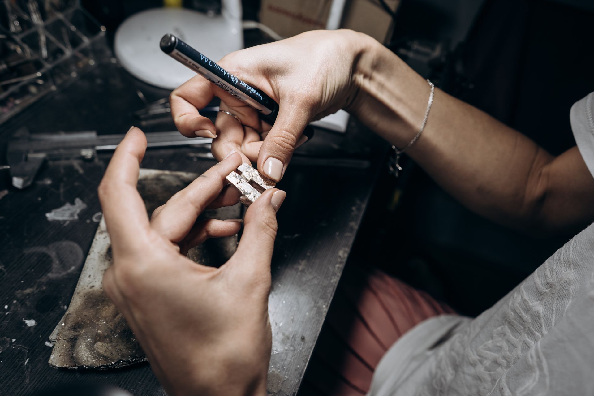 Hands preparing a small item with foil and a pen on a cluttered work surface.