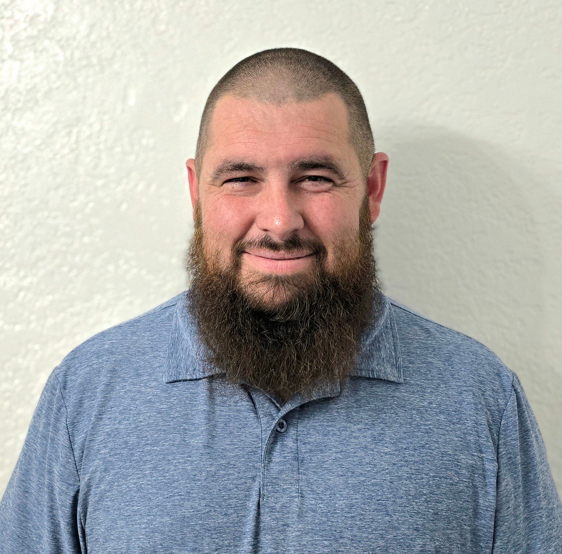 A man with a beard is wearing a blue shirt and smiling for the camera.