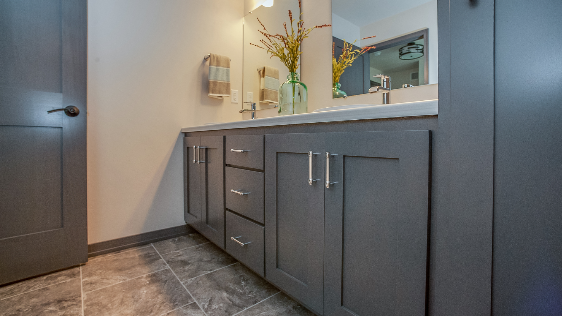 Modern bathroom vanity with gray cabinets, white countertop, mirror, and vase of flowers.