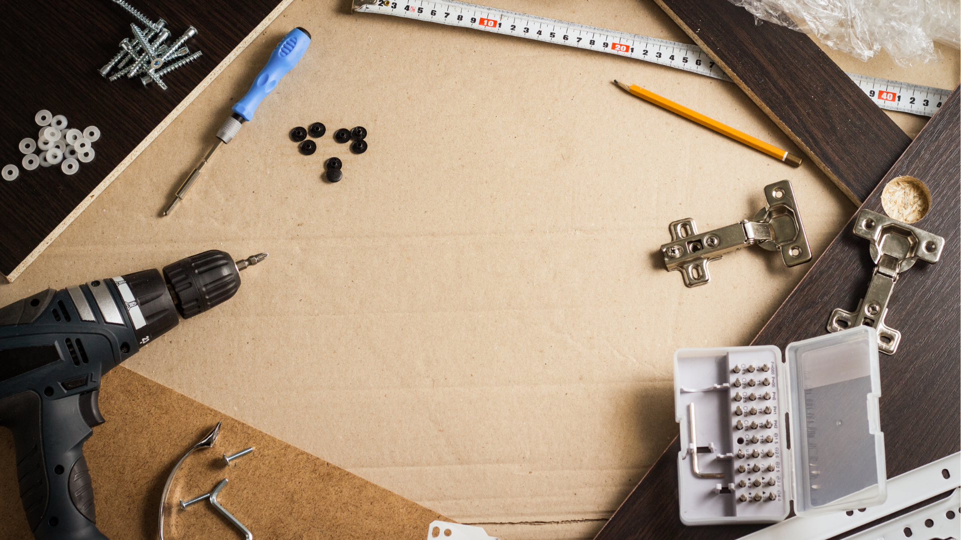 Craft workspace with drill, pencil, ruler, screws, and small parts on a cardboard surface