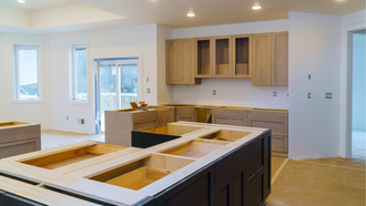 Bright unfinished kitchen with light wood cabinets, white walls, and a central island under construction