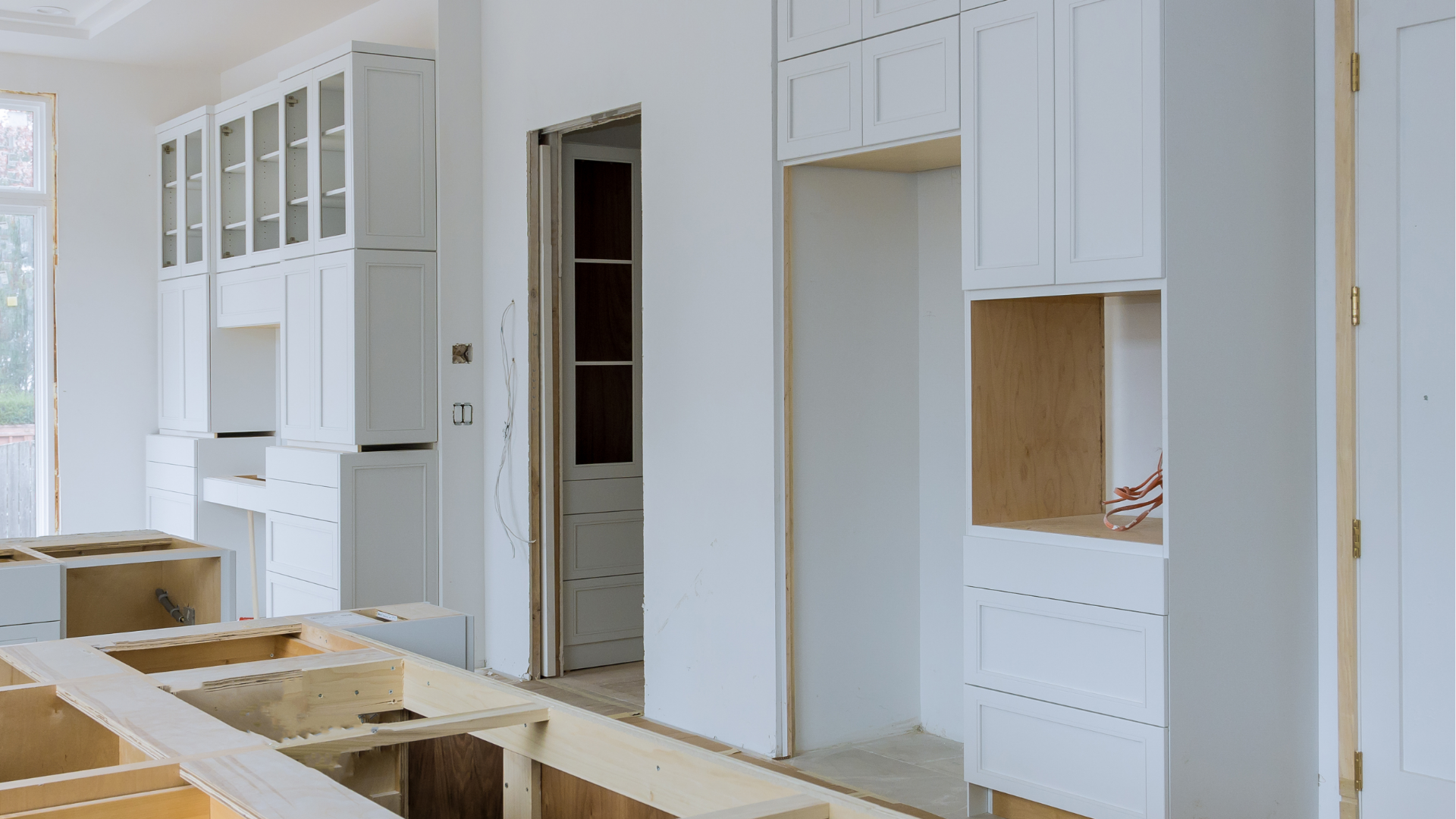 White kitchen cabinets and unfinished countertops in a bright, partially renovated room