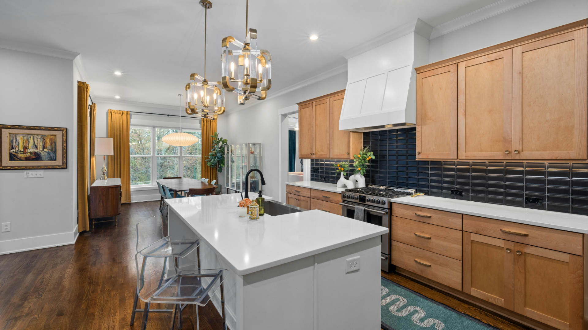 Bright modern kitchen with white island, wood cabinets, dark backsplash, and chandelier lighting