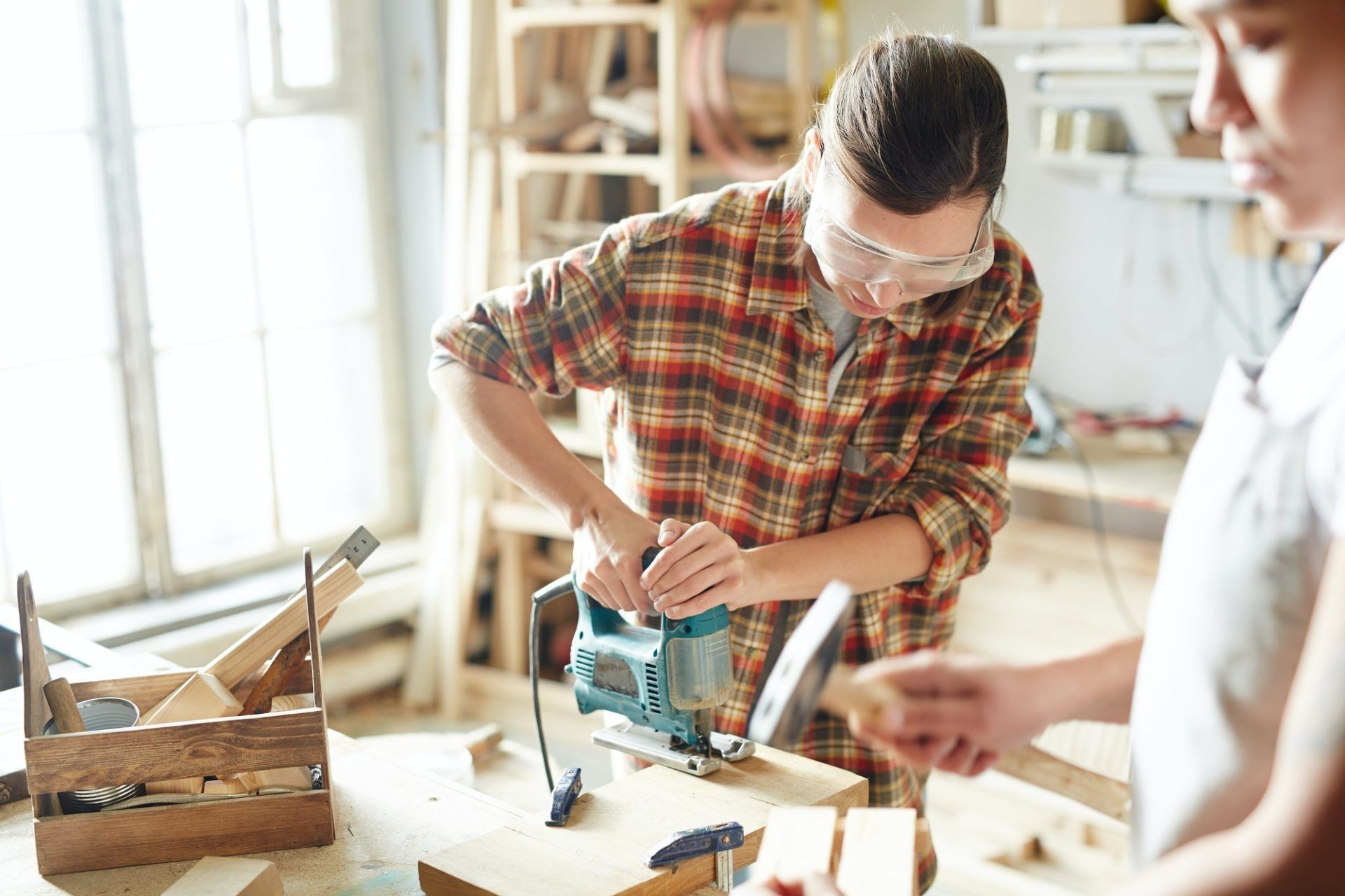 Person using a jigsaw on wood in a bright workshop, with tools and materials nearby