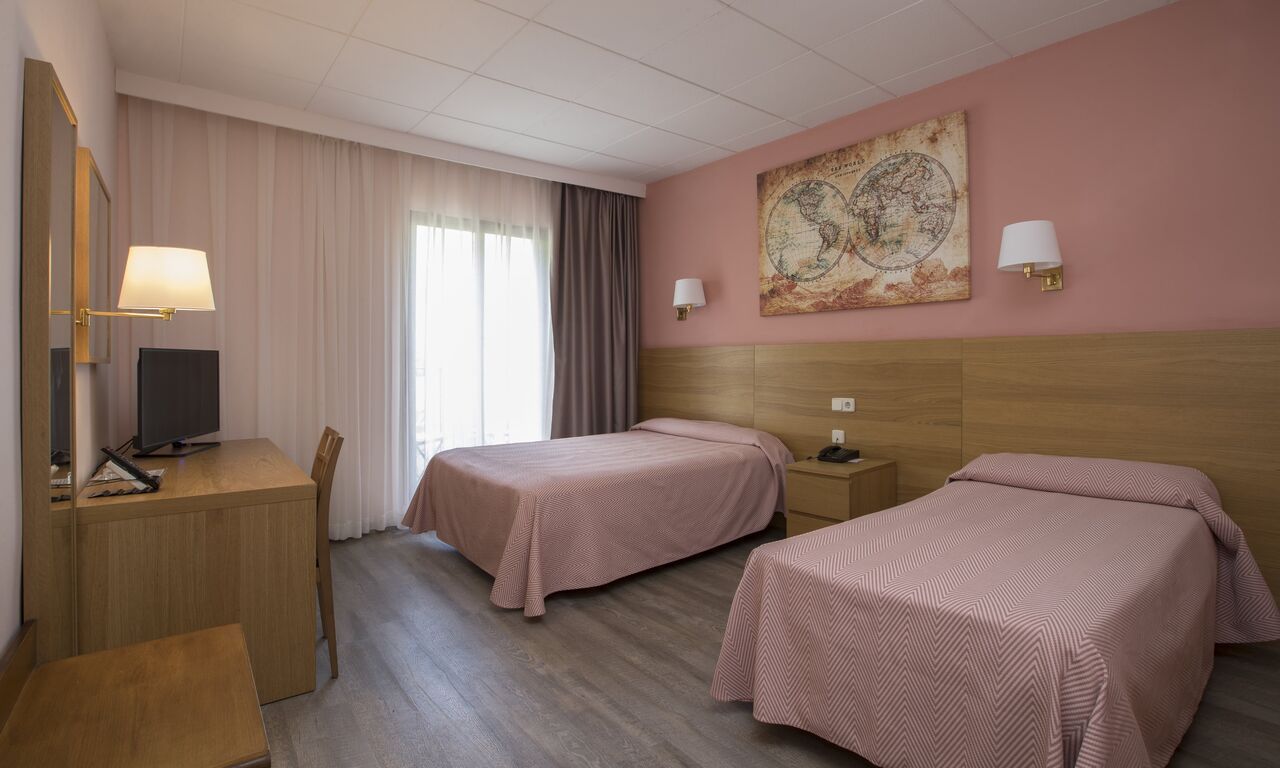 Hotel room with two twin beds, desk, and artwork on a pink wall.