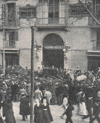People gathered in front of the Grand Hotel building. Black and white photo, circa early 20th century.