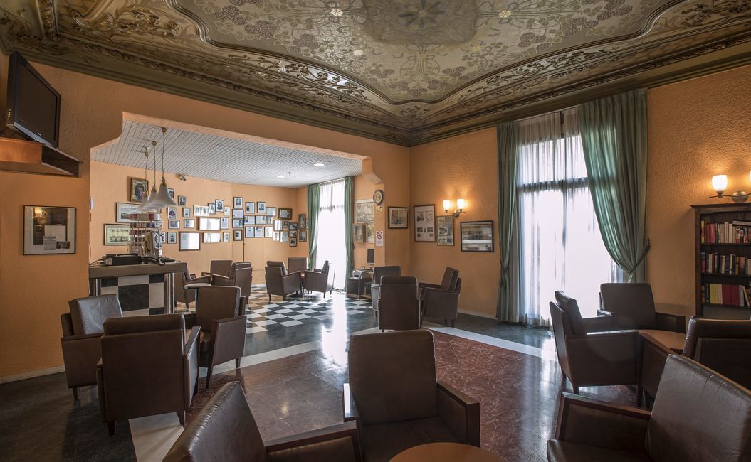 A room with brown chairs, checkered floors, ornate ceiling, and framed photos.