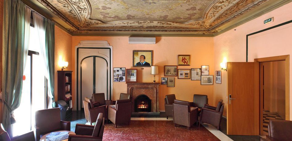 A room with peach walls, patterned ceiling, a fireplace, and several armchairs arranged for conversation.
