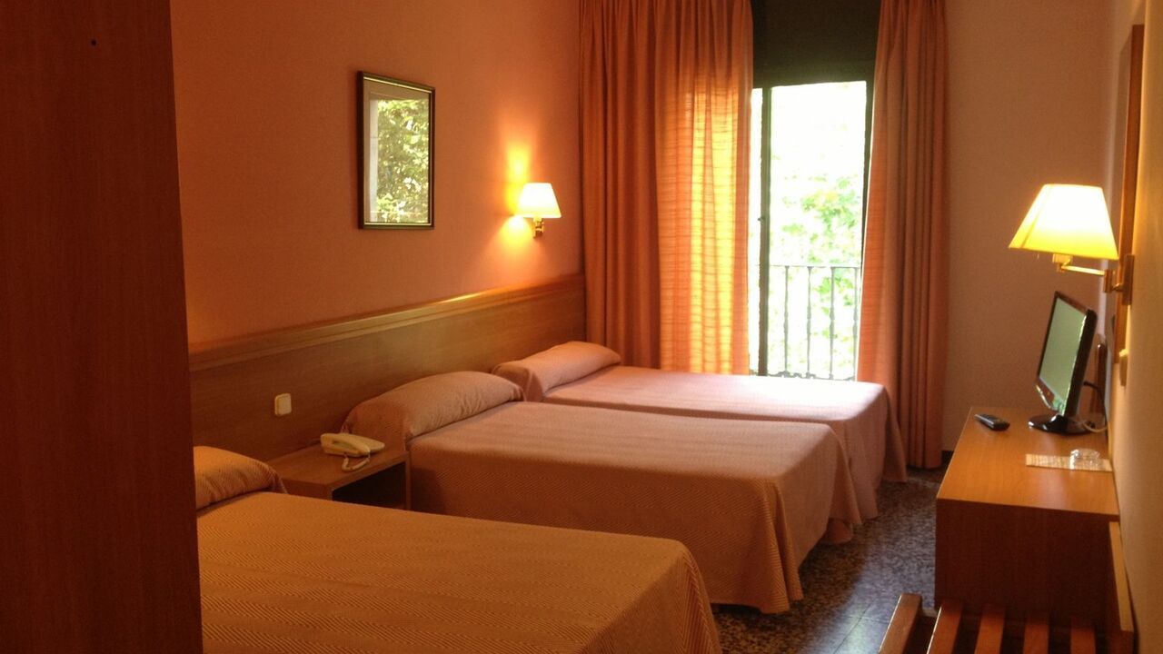 Hotel room with three beds, orange walls, a balcony, and a television.