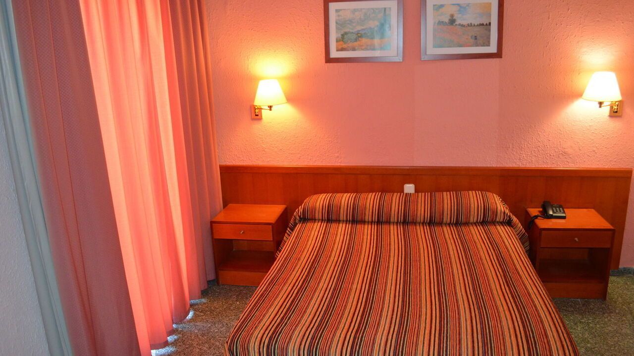 Hotel room with a double bed, nightstands, lamps, and pink walls and curtains.