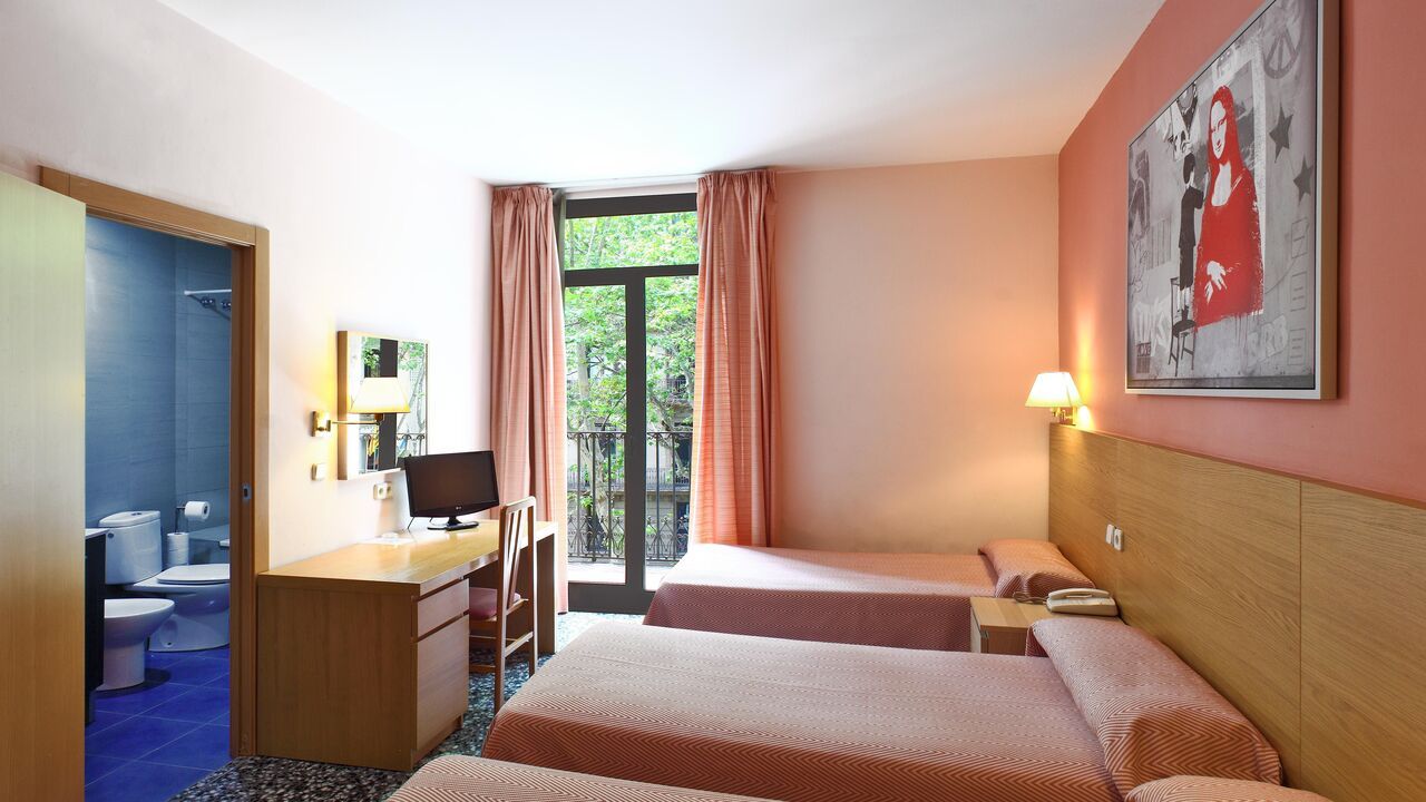 Hotel room with three beds, a desk, a window, and a doorway to a bathroom.