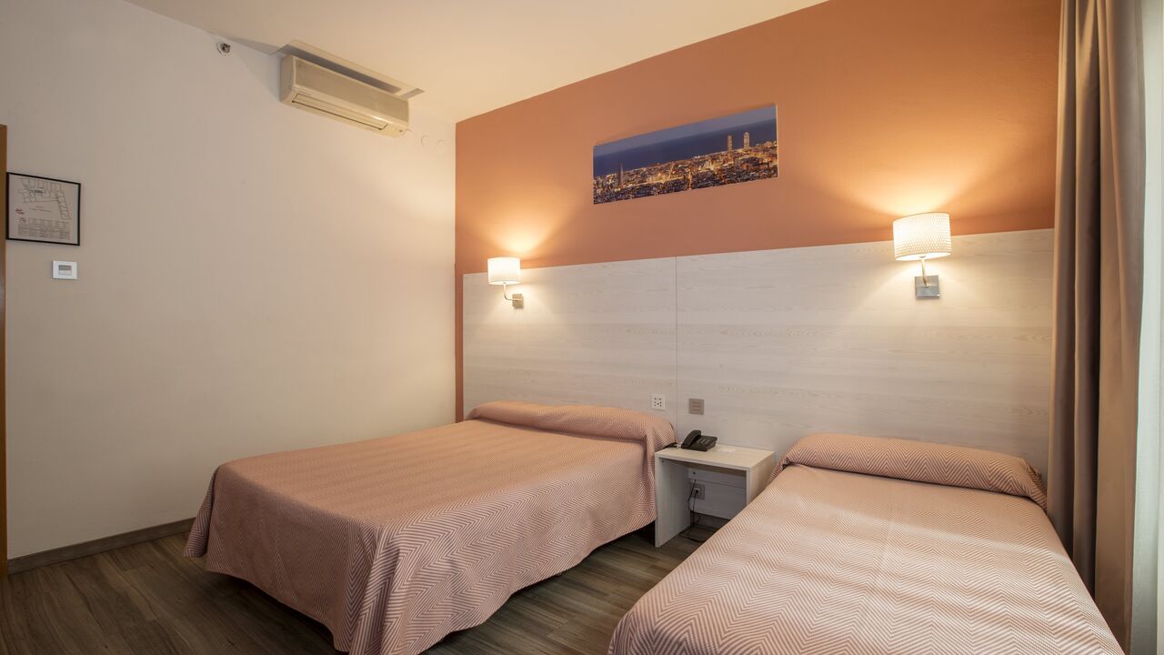 A hotel room with two beds, peach-colored walls, and a cityscape print.