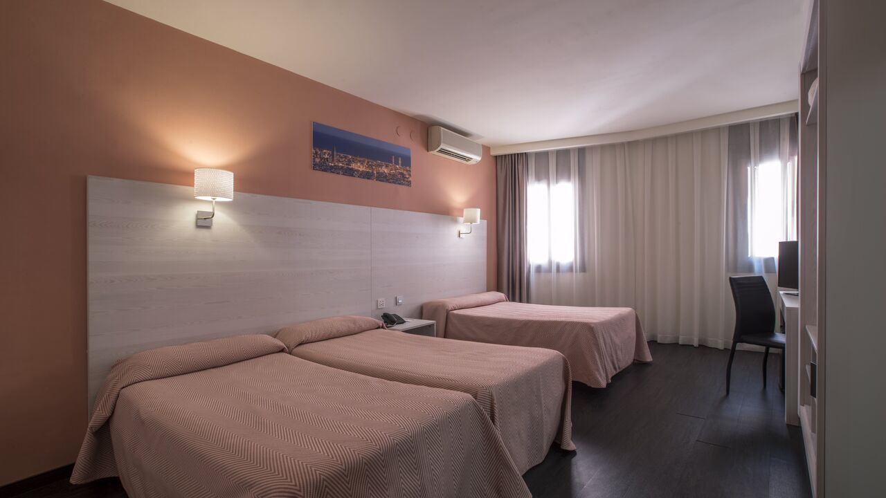 Hotel room with three beds, light pink bedding, brown floor, and artwork on the wall.