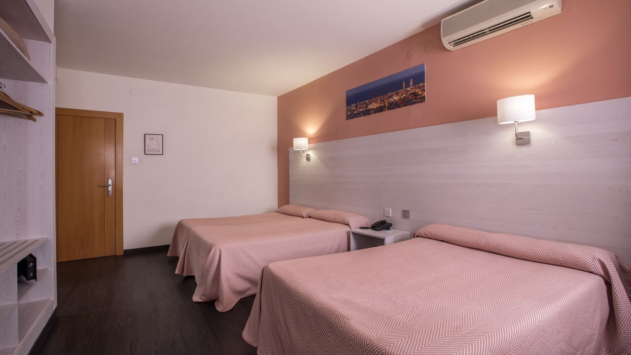 Hotel room with two twin beds, pink linens, wood floor, and a cityscape picture on the wall.